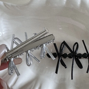 Close-up of silver and black bow hair clips with heart bead details on a ceramic plate