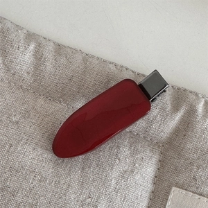 Close-up of a deep red acetic acid hair clip on beige linen, elegant teardrop design