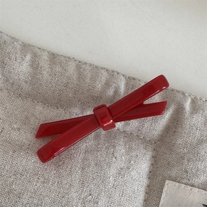 Detailed macro view of the glossy dark red bow hair clip on a textured fabric background