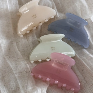 Detailed close-up of colorful acetate hair claws with brand logo on soft fabric background