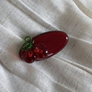 Detailed view of red translucent cherry hair clip with green leaf on white linen fabric
