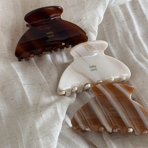 Three acetate hair claws in tortoise and marble patterns on white linen fabric