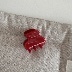 Close-up of a glossy dark red acetate hair claw clip on a beige textured linen surface