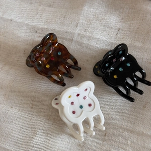 Detailed view of acetate flower hair clips with colorful rhinestones on beige linen