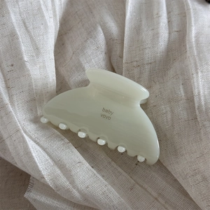 Detail view of cream acetate hair claw clip with baby vovo text on linen fabric