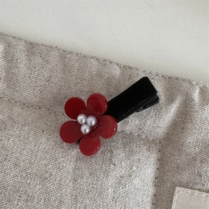Close-up of red flower hair clip featuring white pearls and black velvet band texture