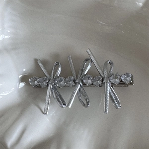 Macro detail of silver bow hair clip with sparkling rhinestones on a white plate