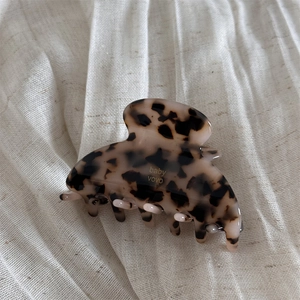 Detail view of acetate tortoise shell hair claw clip with golden baby vovo logo on linen