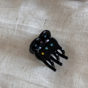 Close-up of a black acetate flower hair claw clip with colorful rhinestones on fabric