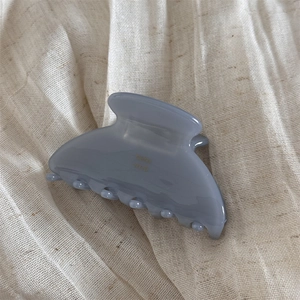 Macro detail of glossy jelly texture claw clip in grey blue on soft linen background