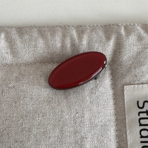Detail shot of smooth dark red oval acetate hair clip on a beige linen fabric background