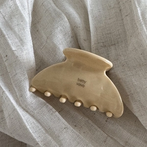 Detailed close-up of a glossy cream acetate hair claw clip on soft textured linen fabric