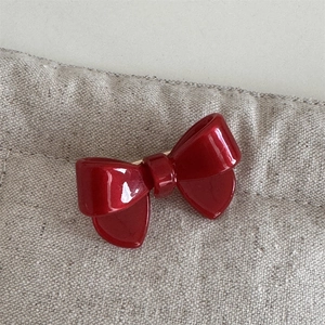Detailed close-up of glossy red acetate bow hair clip on natural beige fabric texture