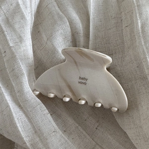 Detail of cream marble cellulose acetate hair claw clip on soft linen fabric texture