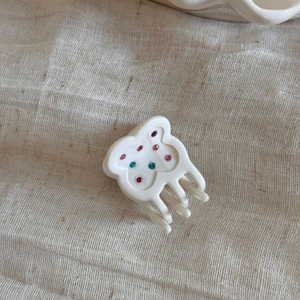 Detail showing a white acetate bear hair claw clip with pink and teal rhinestones
