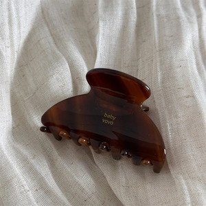 Detailed view of brown tortoiseshell hair claw with golden baby vovo logo on linen