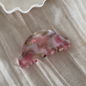 Detail view of pink and white marble acetate hair claw with elegant gold label