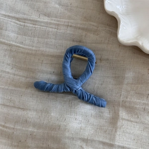 Detailed view of a blue denim wrapped metal hair claw clip on beige fabric background