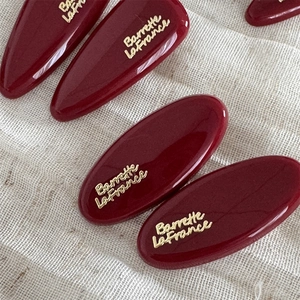 Macro view of dark red glossy hair clips with golden letters on beige textured fabric