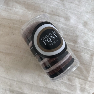 Neutral velvet hair scrunchies set in clear cylinder jar on linen fabric