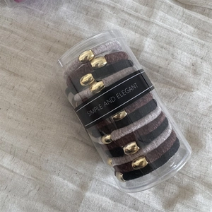 Elastic velvet hair ties in neutral tones with gold accents in a clear cylinder case