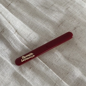Close-up of a burgundy hair clip with gold Barrette LaFrance lettering on fabric