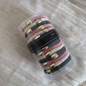 Close-up of velvet hair ties in pink, white, and grey with gold buckle in a clear tube