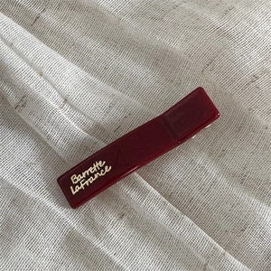 Detail showing dark red rectangular hair clip with gold Barrette La France lettering