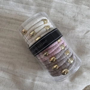 Close-up of velvet scrunchies in cream and pink with gold metal charms in a clear box