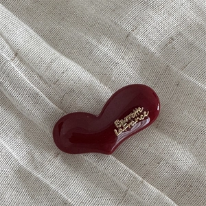Detail view of a burgundy resin heart hair clip with gold lettering on linen fabric