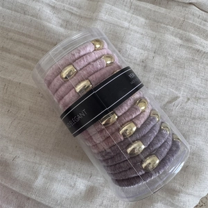 Detailed view of pink and grey velvet elastic hair ties with gold metal buckles in a clear box