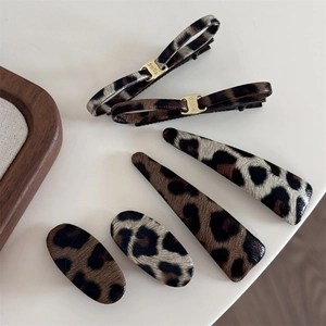 Detail of six leopard print hair clips featuring golden Smile charms on a minimalist background
