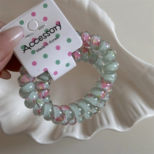 Detail of mint green spiral hair tie with pink floral pattern on cardboard