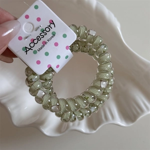 Close-up of green floral spiral hair coil with Accessory tag on shell tray