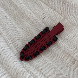 Detail of red and black woven leather wrapped alloy hair clip on soft fabric background