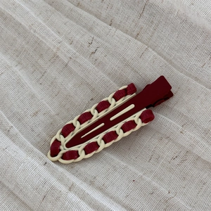 Detailed view of vintage burgundy leather woven alloy hair clip on a white linen surface