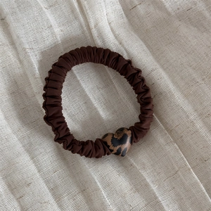 Dettaglio del ciondolo a cuore leopardato su elastico per capelli marrone testurizzato