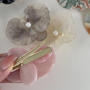 Detailed close-up of acetate orchid hair clip with faux pearl and metal fastener back