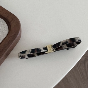 Detail of leopard print fabric bow hair clip featuring a gold buckle engraved with Smile