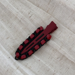 Close-up of wine red leather hair clip with woven black chain and ribbon detail