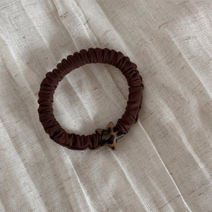 Dettaglio dello scrunchie marrone scuro con ciondolo a stella stampa leopardata