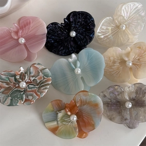 Flat lay of eight colorful orchid-shaped hair clips with pearl centers made of acetate fiber