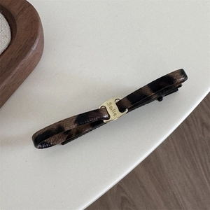 Macro shot of leopard print fabric hair clip with a gold buckle engraved with the word Smile