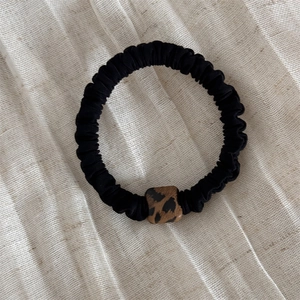 Dettaglio di un elastico per capelli nero plissettato con fibbia leopardata quadrata