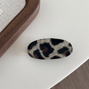 Close-up of leopard print hair clip with smooth acetate texture on a minimal wooden base
