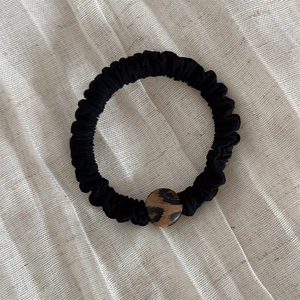 Dettaglio dell'elastico scrunchie nero plissettato con ornamento geometrico maculato