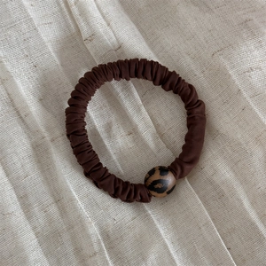Dettaglio di un elastico marrone scuro con perla leopardata su sfondo in tessuto beige