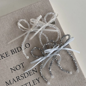 Elegant beaded bow hair clips in white and grey silver set on textured linen background