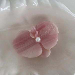 Detail of pink acetate orchid hair clip with white pearl center on ceramic tray