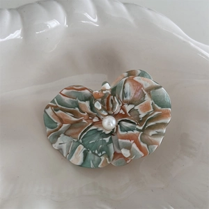 Detailed close-up of marble acetate orchid hair clip with pearl center on a white shell plate